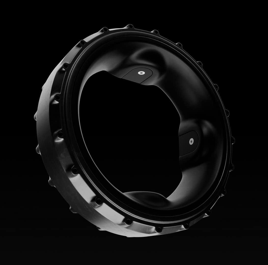 A close-up of a black, circular mechanical part with a rugged, knobby edge, photographed against a black background. The ring has two flat sections with small circular holes.